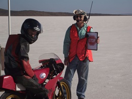 Man on a red motorcycle waiting infront of another man holding a stop sign